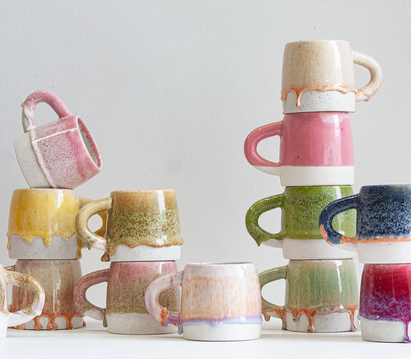 a group of handmade ceramic mugs by rhiannon gill, various colours are stacked on top of each other to show a diverse range